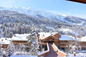 A lodge with a central building, surrounded by snow-covered trees and mountains in the background.