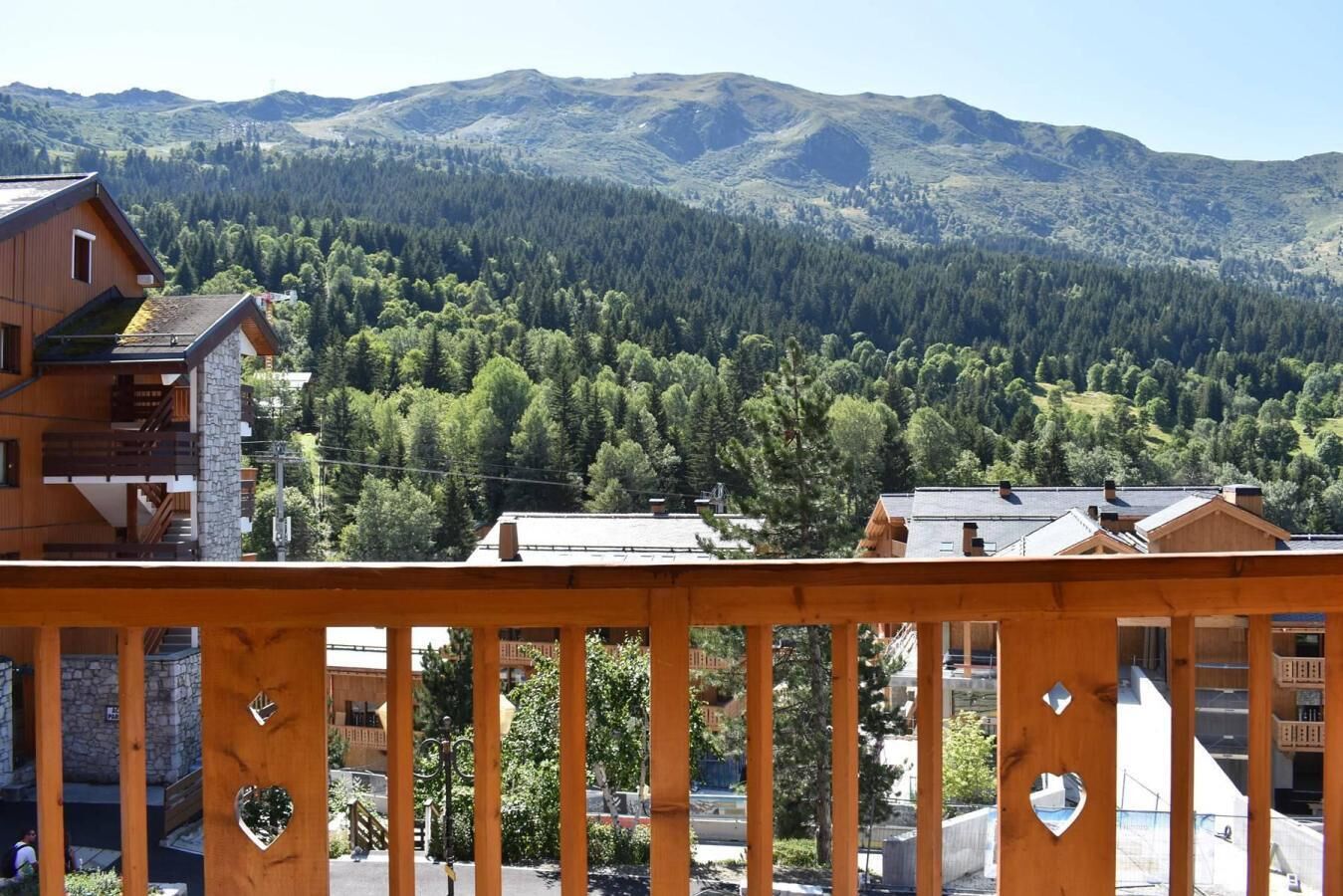 Un balcón de madera con recortestá forma de corazón, con vistas a un valle boscoso y montañas al fondo.