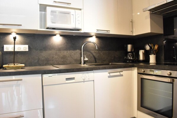 A modern kitchen with white cabinets, a Bosch dishwasher, a microwave, a stainless steel sink, and an oven.