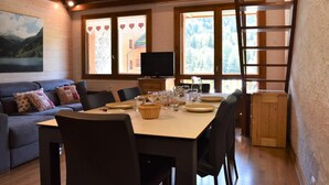 A cozy dining area with a wooden table set for four, a sofa with cushions, and a TV on a wooden cabinet.