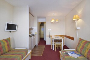 Habitación de hotel compacta con kitchenette, zona de comedor y televisor montado en la pared.