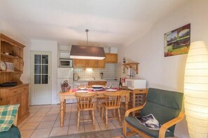 Une cuisine compacte avec des meubles de rangement en bois, une table à manger avec des chaises et un fauteuil vert.