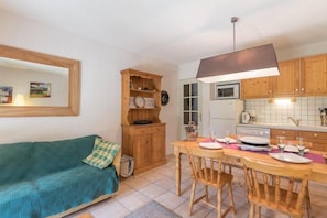 Une cuisine chaleureuse avec des meubles en bois, une table à manger pour quatre personnes et un canapé dans le salon attenant.