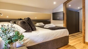 A modern bedroom with a large bed, a flat-screen TV mounted on the wall, and a wooden floor.