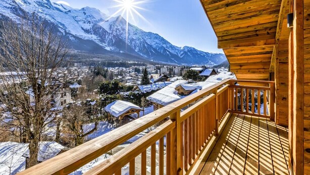A wooden balcony with a view of snow-covered mountains and a town below.