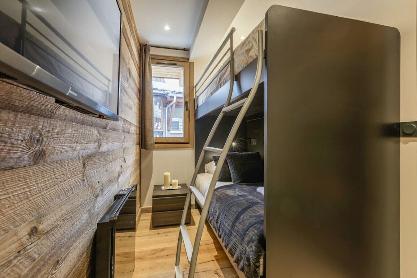 Habitación compacta con literas, una mesita de noche pequeña con velas y una ventana que deja entrar luz natural.