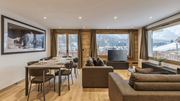 Una sala de estar moderna con comedor, ventanas amplias que ofrecen vistas a una montaña nevada y un televisor de pantalla plana.