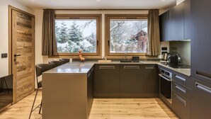 Una cocina moderna con una isla central, armarios oscuros y vistas a un paisaje nevado a través de amplios ventanales.