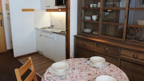 Een kleine keuken met witte kasten, een magnetron en een vaatwasser. Er staat een eettafel met een tafelkleed en bestek.