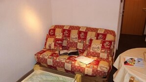 Een gezellige kamer met een gewatteerde bank, een klein houten tafeltje met een kaart en een bed met een wit laken.