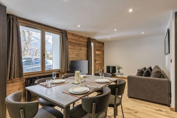 A dining area with a wooden table set for four, a sofa, and a TV in the background.