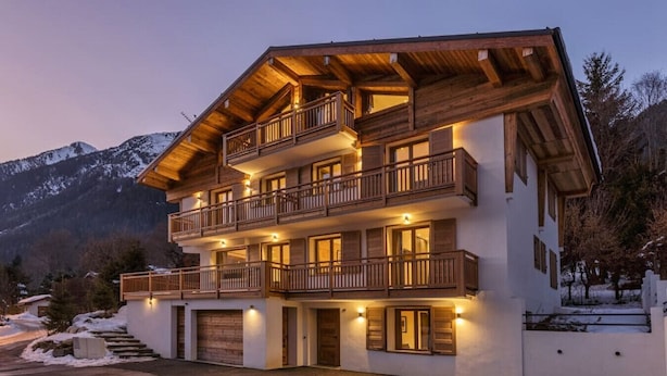 Eine mehrstöckige Holzhütte mit Balkonen, einer Garage und Blick auf schneebedeckte Berge.