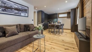 Ein modernes Wohnzimmer mit Sofa, einem kleinen Tisch mit Vase, einer Essecke mit Tisch und Stühlen, einer Küche und einem Fernseher.