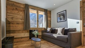 Un salón acogedor con una pared de madera, un sofá gris, una mesita con un jarrón y una ventana con vistas a montañas.