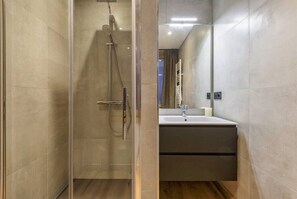 Bathroom features a glass-enclosed shower with handheld showerhead and wall-mounted faucet, alongside a sink with a mirror.