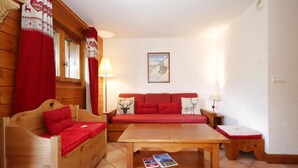 A cozy room with a wooden sofa, a wooden table, and a red patterned couch.