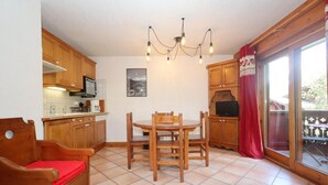 A kitchen with wooden cabinets, a dining table with chairs, a chandelier, and a television.