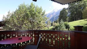 A balcony with a red table and chairs, a decorative metal fence, and a mountainous landscape in the background.