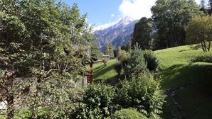 A mountainous landscape with a clear sky, lush greenery, and a small building with a red roof.