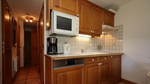 A compact kitchen with wooden cabinets, a built-in microwave, a coffee maker, and a dishwasher.