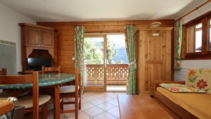 A wooden cabin interior with a dining table, chairs, a sofa, and a television.