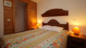 A bedroom with a wooden wardrobe, a bed with floral bedding, and two bedside lamps.