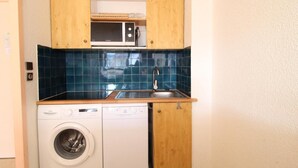 Une cuisine compacte équipée d’un lave-linge, d’un four à micro-ondes et de meubles de rangement en bois.