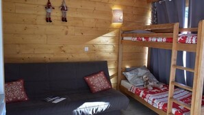 A cozy cabin room with a wooden wall, a bunk bed, a sofa, and a small table. - 100m from shops, 2nd floor, view mountain, balcony, parking, tv, ski locker, 18m², Montgenèvre (Montgenèvre)