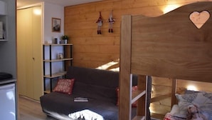 A cozy room with a wooden headboard, a grey sofa with red cushions, a small bookshelf, and a bed with a patterned blanket. - 100m from shops, 2nd floor, view mountain, balcony, parking, tv, ski locker, 18m², Montgenèvre (Montgenèvre)