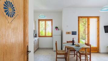 Zona de menjador amb taula, cadires i vistes a la vegetació exterior.