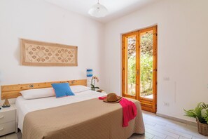 Une chambre à coucher comprenant un lit, une table de chevet, une lampe fixée au mur, une fenêtre donnant sur un paysage verdoyant et un élément décoratif mural.