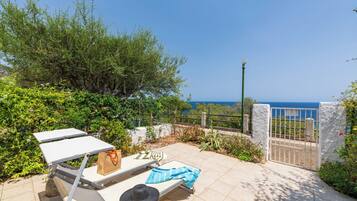 A sunlit outdoor seating area with a view of the sea, a metal gate, and a white wall.