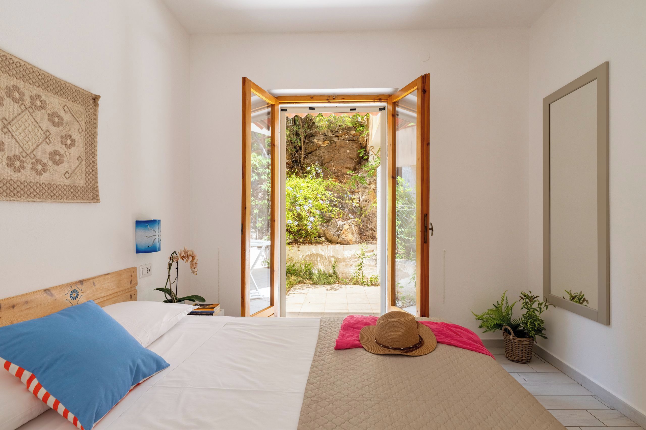 A bedroom with a bed, a window, a door, and a view of a garden.
