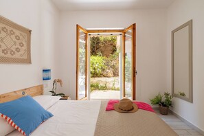 A bedroom with a bed, a window, a door, and a view of a garden. - Home Nido (Cala Gonone)
