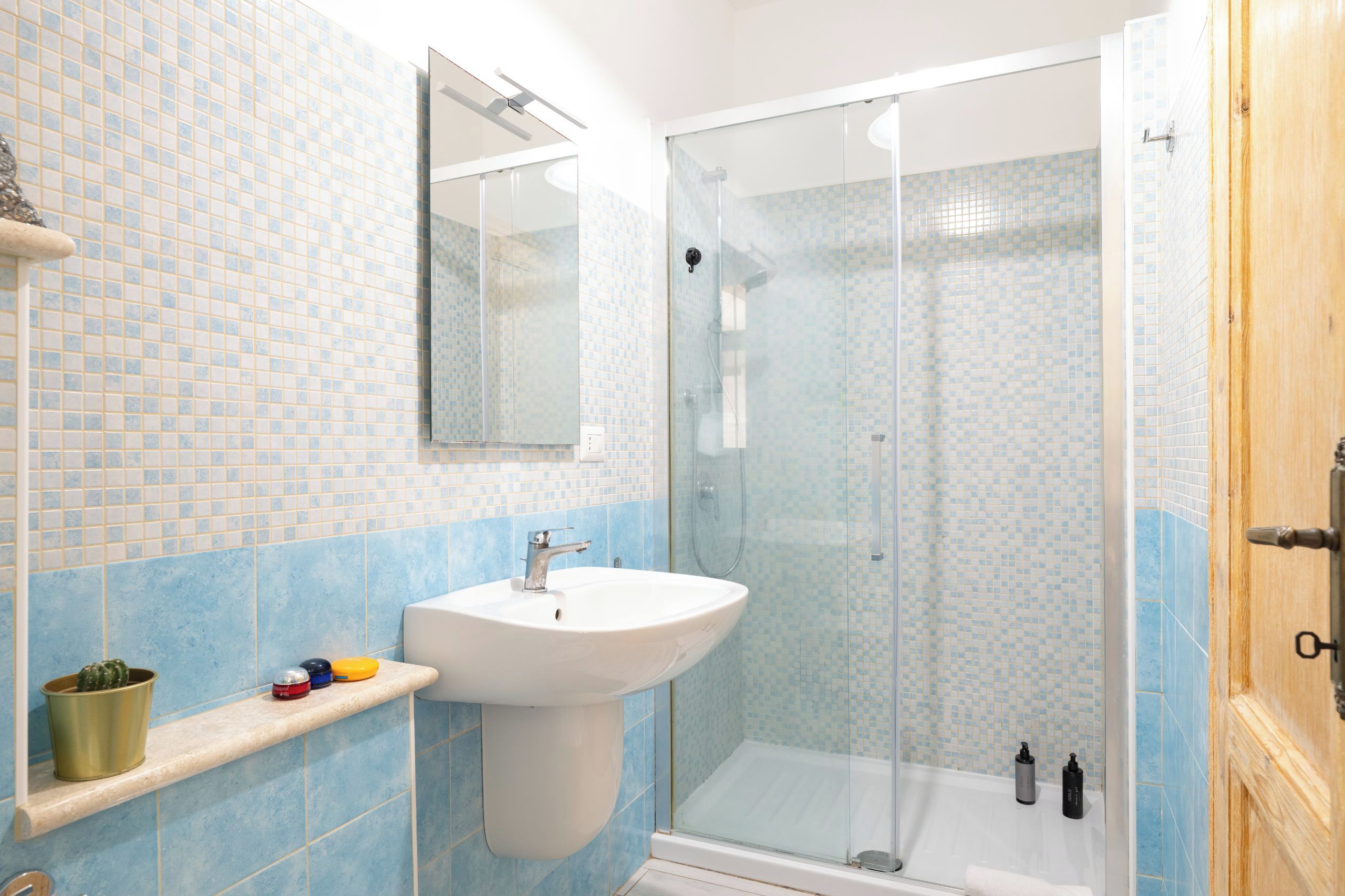 Un bagno con un lavandino bianco, una cabina doccia in vetro e una parete rivestita di piastrelle.