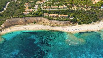 Vista aérea de una zona costera con playa, aguas azules cristalinas y una área residencial con casas.