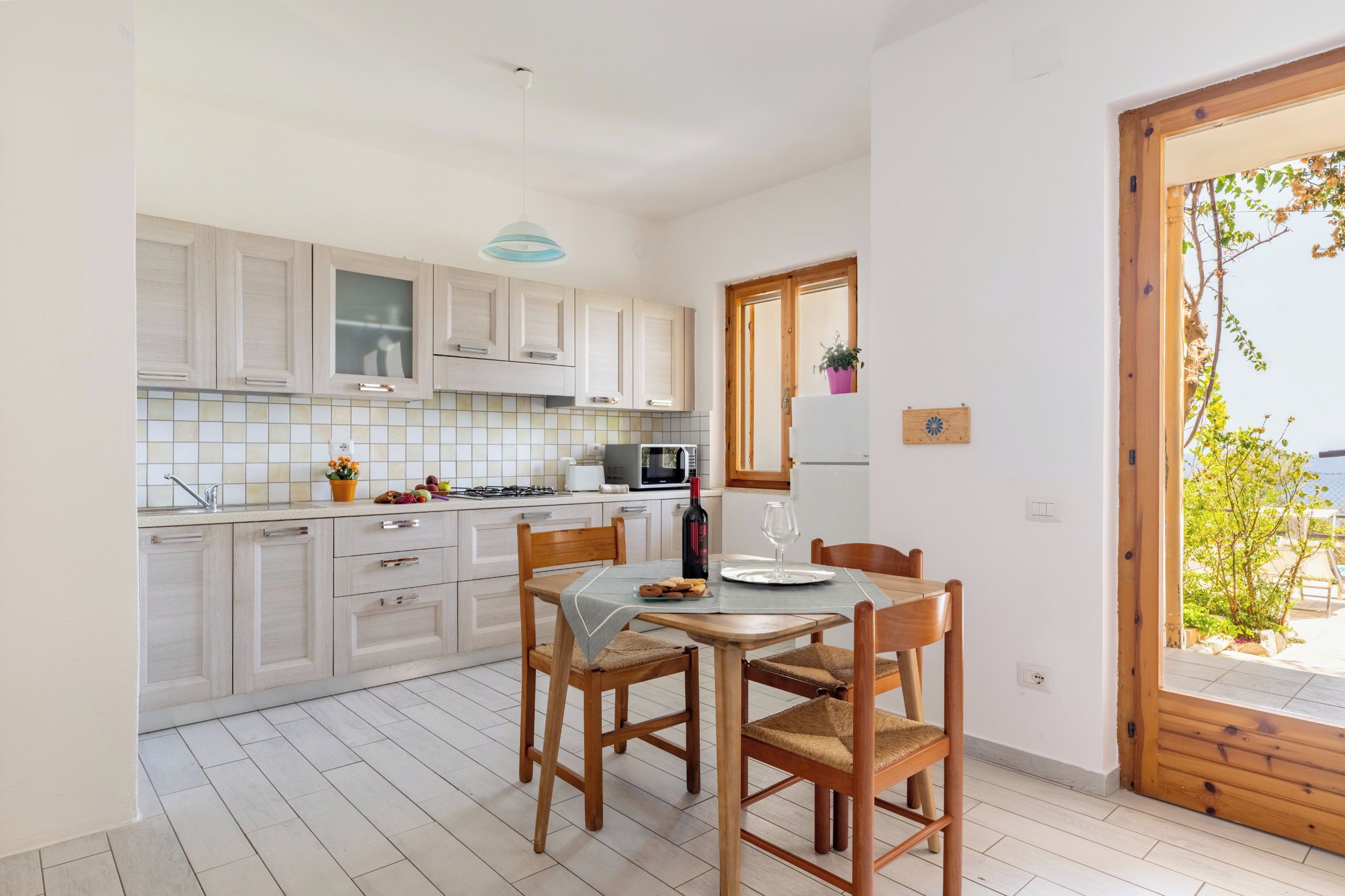 A modern kitchen with wooden cabinets, a dining table with chairs, and a view through a wooden door.