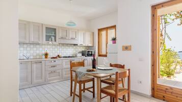 A modern kitchen with wooden cabinets, a dining table with chairs, and a view through a wooden door.