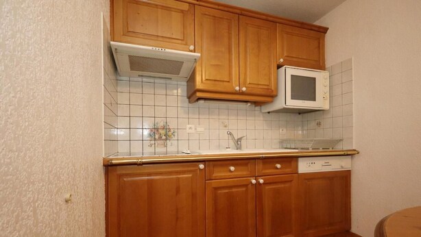 Een keuken met houten kastjes, een magnetron en een betegelde spatwand.