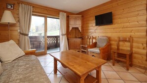 Ein Interieur einer Holzhütte mit einer Couch, einem Holztisch, einem an der Wand montierten Fernseher und einer Glastür, die zu einem Außenbereich führt.