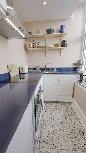 A compact kitchen with a dark countertop, white cabinets, a built-in oven, and a backsplash.