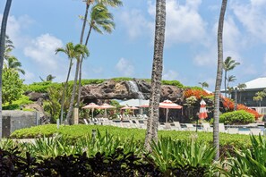 A resort with a pool, palm trees, and a rocky backdrop. - Beautiful Oceanfront Resort With Walk Out room to the 4 Resort Pools and Beach (Lihue)