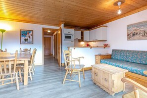Ein gemütliches Zimmer mit Holzbalkendecke, einem Esstisch mit Stühlen, einer Couch und einer Küchenzeile mit Schränken und einer Mikrowelle.