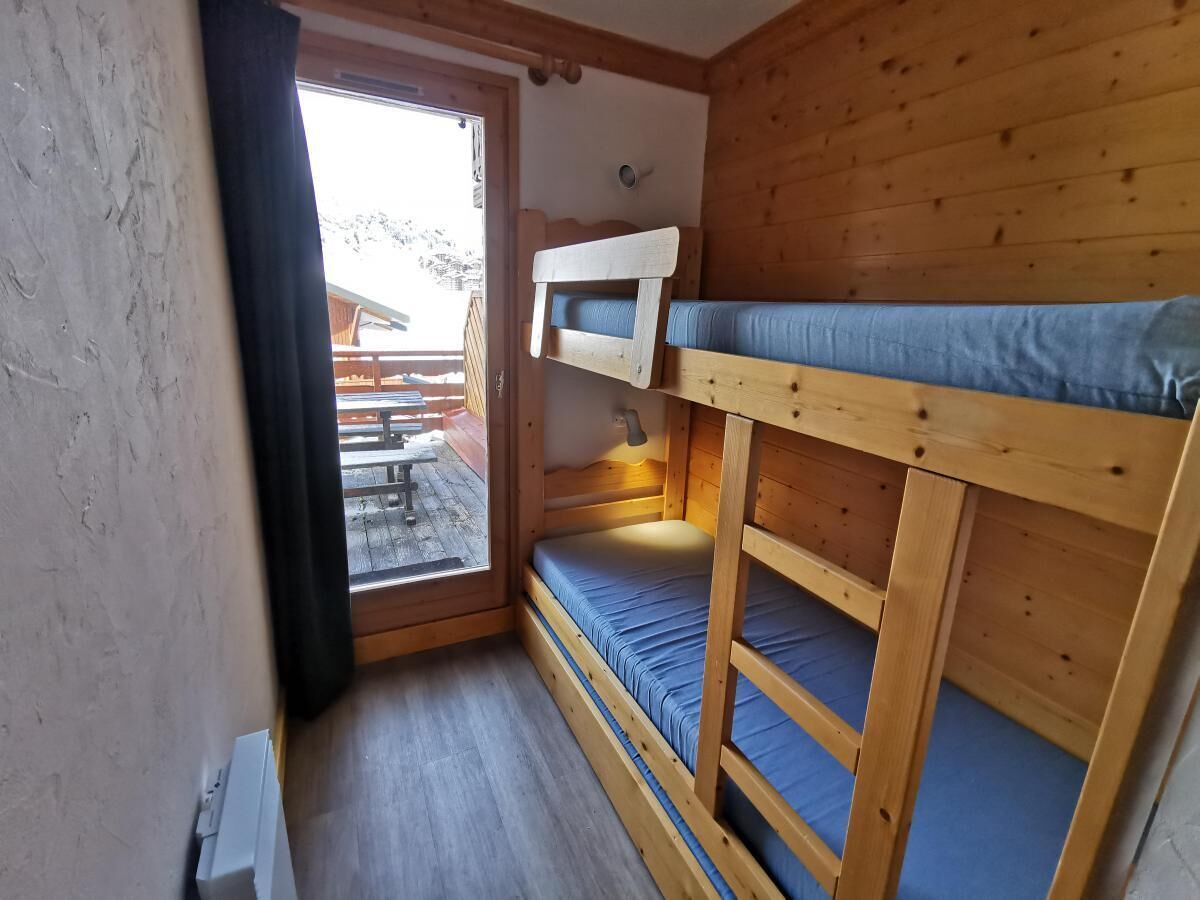 A small, wooden cabin with bunk beds, a window, and a view of an outdoor deck.