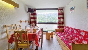 Un cuarto acogedor con una mesa de comedor preparada para cuatro personas, un sofá rojo y vistas a las montañas a través de un amplio ventanal.