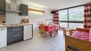 Una cocina compacta con electrodomésticos modernos, un comedor con mantel rojo y una cama con manta estampada.