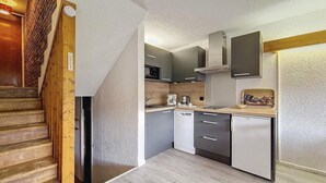 Una cocina compacta con armarios grises, lavavajillas, microondas y refrigerador pequeño.