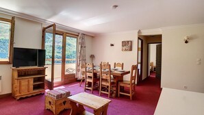 A cozy living room with a wooden TV stand, a dining table with chairs, and a large window with curtains. - 200m from ski slopes, Ground floor, balcony, tv, 50m², Les Menuires (Les Menuires)
