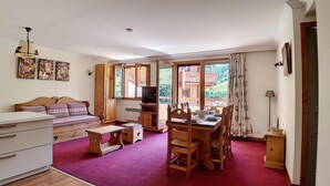 A cozy room with a wooden bed, a dining table with chairs, a TV, and large windows offering a view of the outdoors. - 200m from ski slopes, Ground floor, balcony, tv, 50m², Les Menuires (Les Menuires)