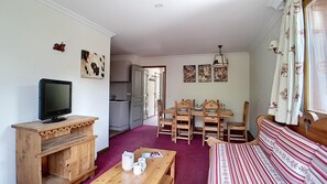 Un salón acogedor con televisor, muebles de madera, una mesa de comedor con sillas y un sofá.